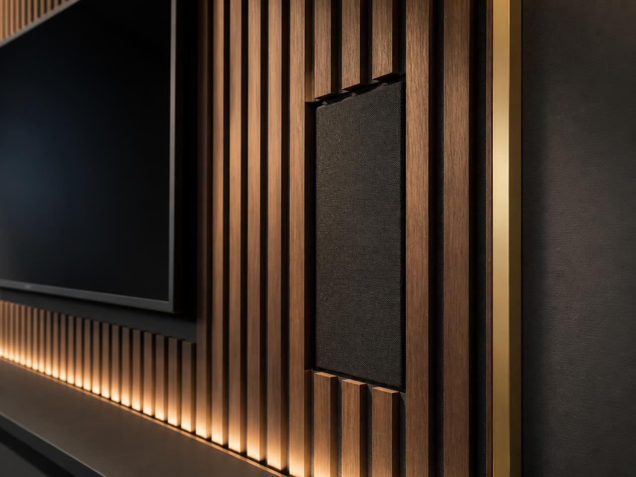 Detail of the AV wall: walnut battens over black acoustic felt with a flush fabric-grille speaker and brass shadow gap